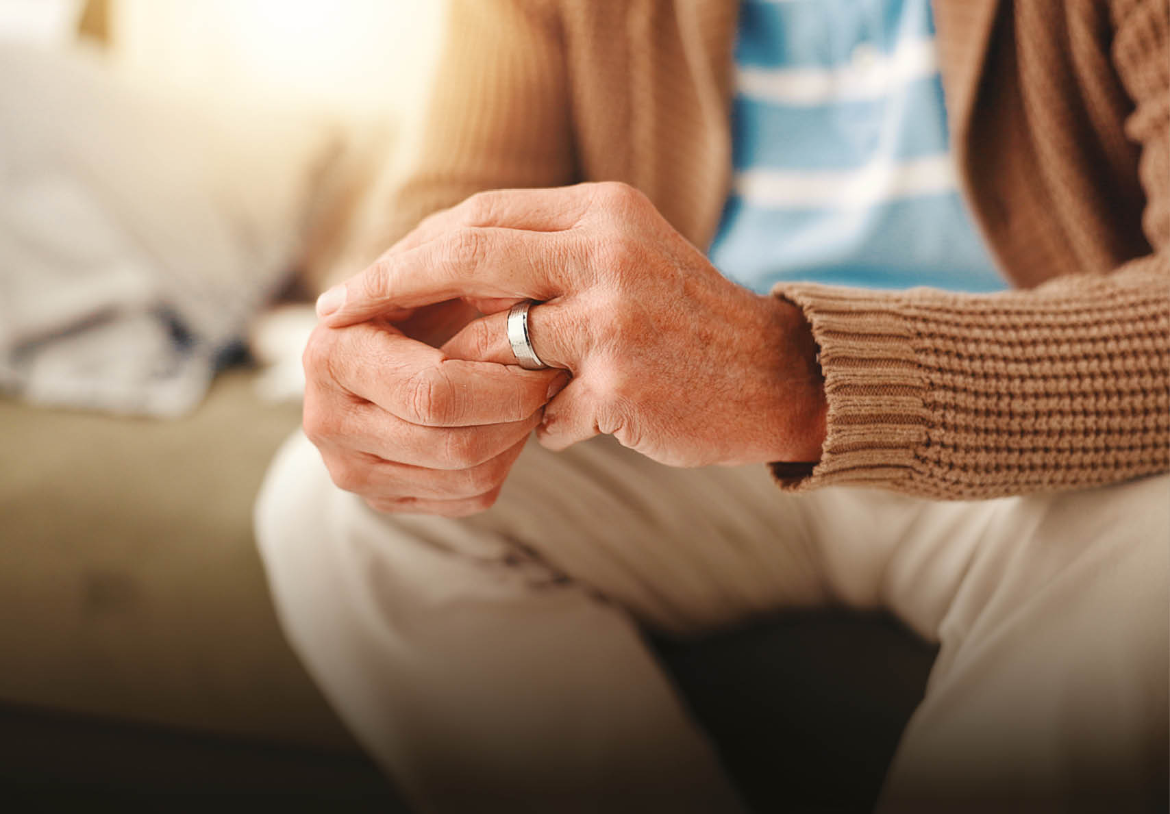 A man wearing a brown sweater and white pants with a wedding ring on his left hand. Description generated by AI