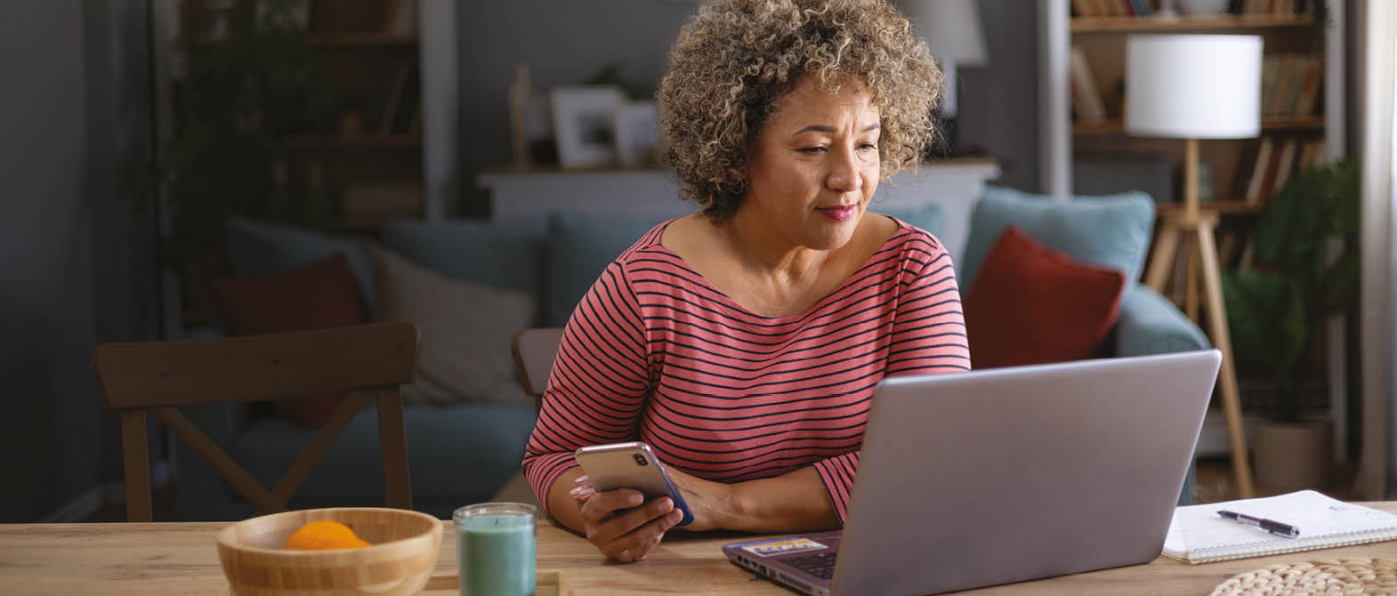 Smiling mid adult woman working on a computer while using mobile phone at home.