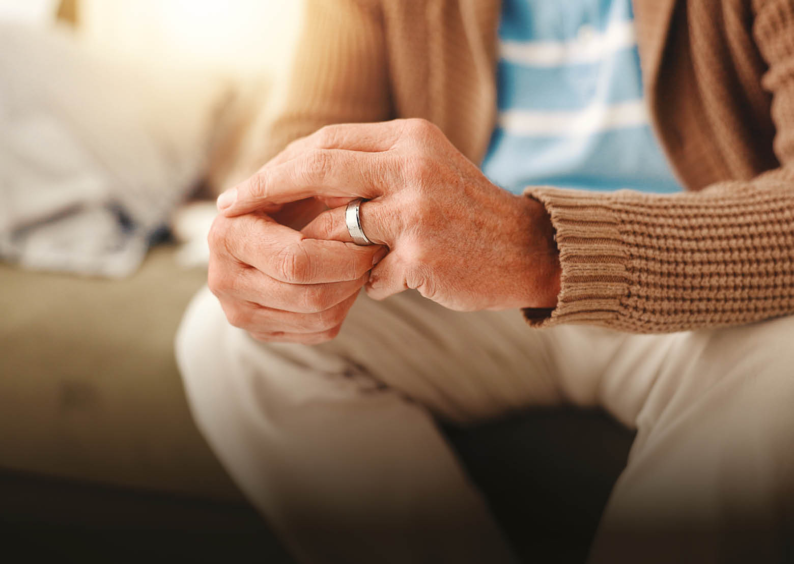 A man wearing a brown sweater and white pants with a wedding ring on his left hand. Description generated by AI