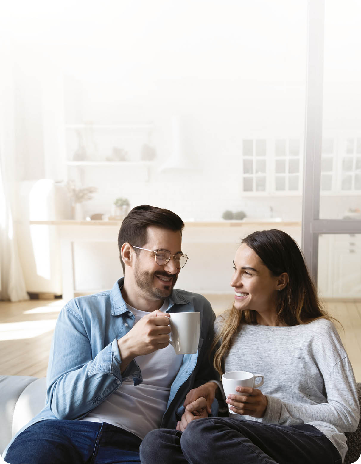 Happy young couple husband and wife relaxing on sofa in modern home living room talking laughing holding cups drinking tea bonding enjoying pleasant conversation romantic leisure lifestyle at home