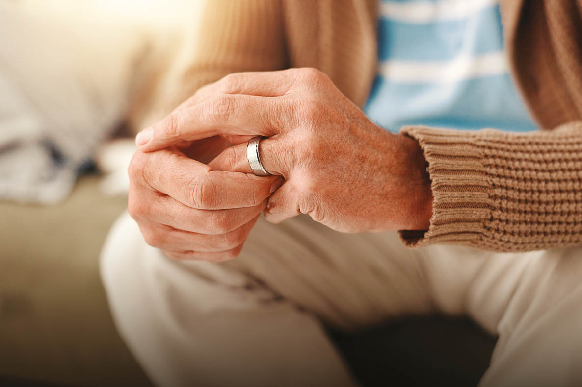 A man wearing a brown sweater and white pants with a wedding ring on his left hand. Description generated by AI