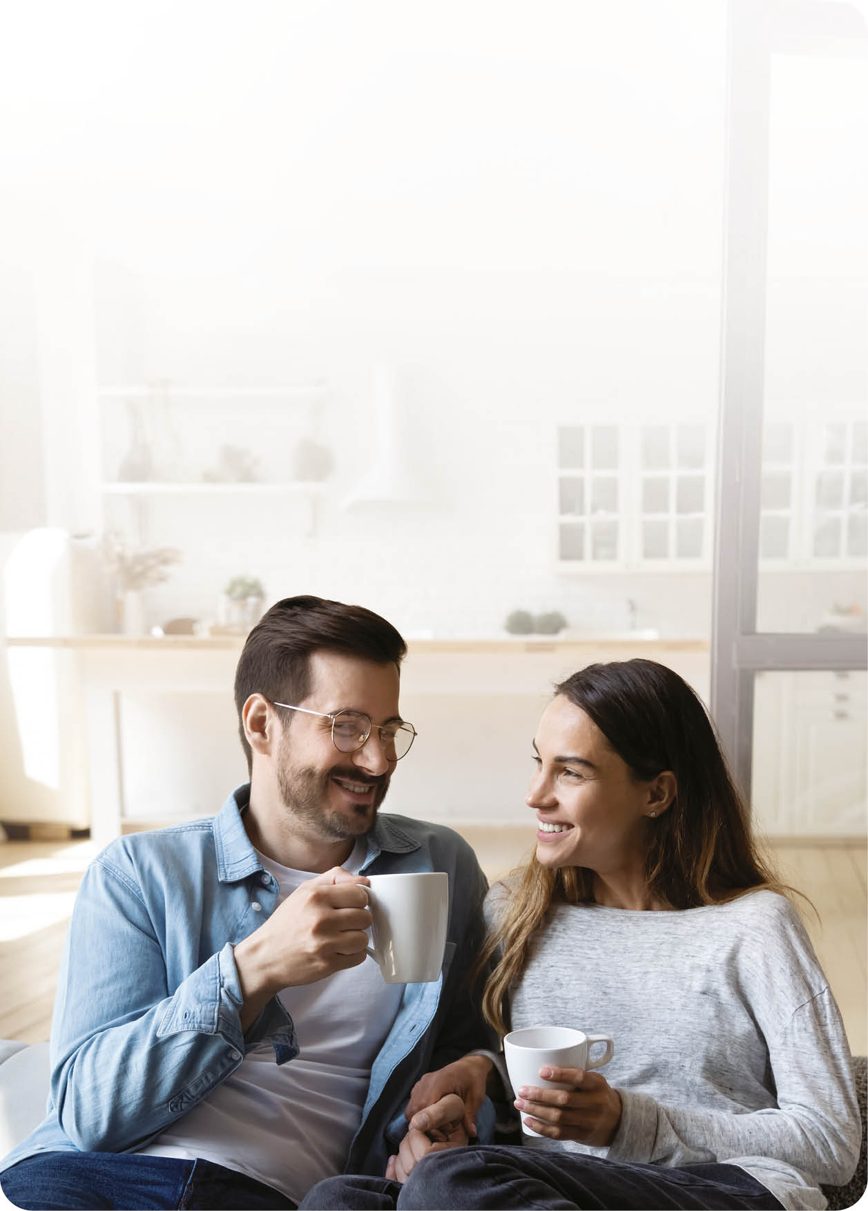 Happy young couple husband and wife relaxing on sofa in modern home living room talking laughing holding cups drinking tea bonding enjoying pleasant conversation romantic leisure lifestyle at home