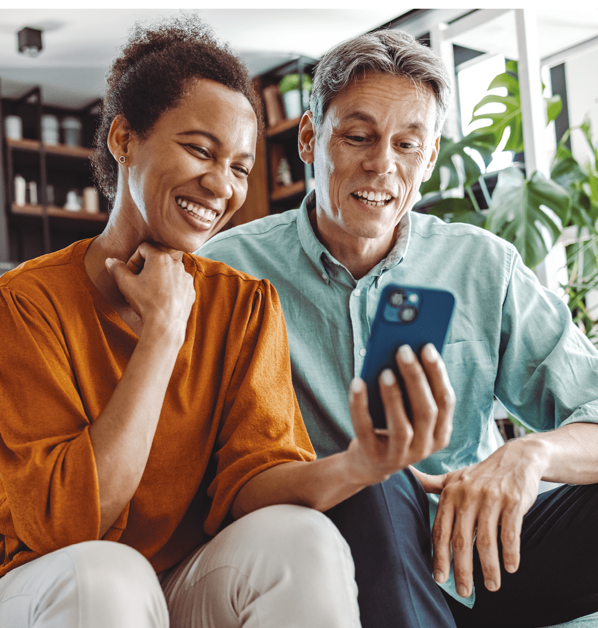 A beautiful African-American woman and a good-looking man sitting in the living room. They are looking at the smart phone and smiling