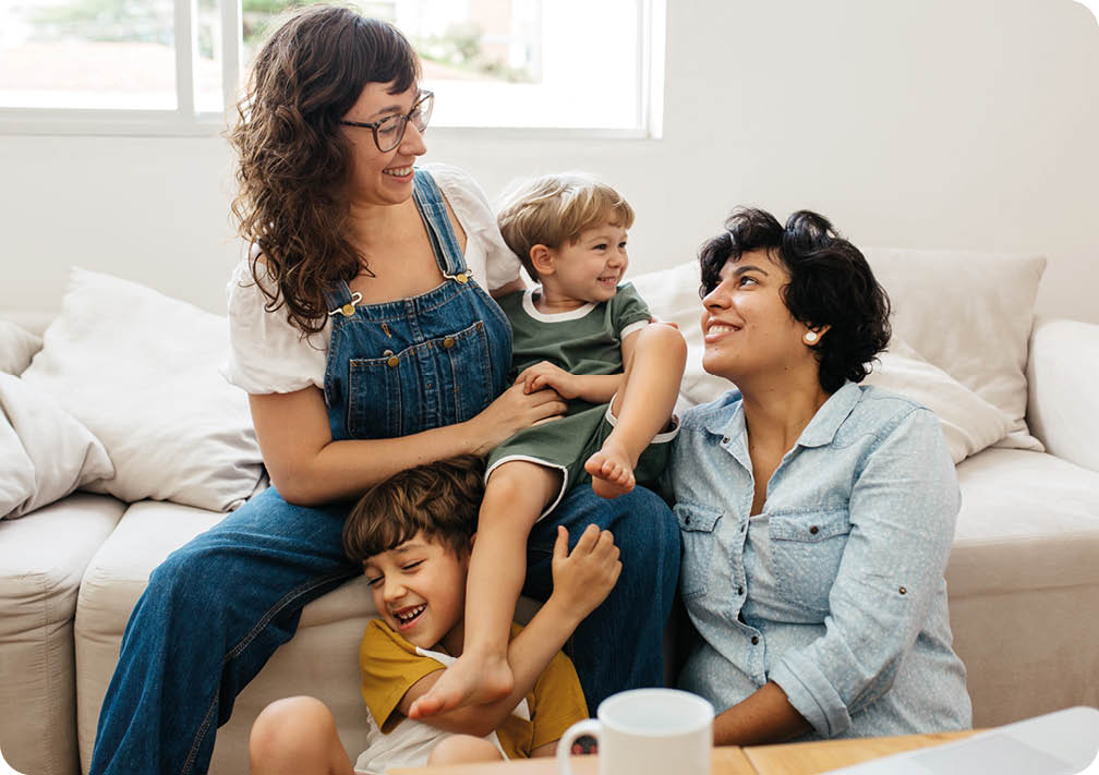 Happy lesbian couple playing with their children at home. Beautiful family of four having great time together indoors.
