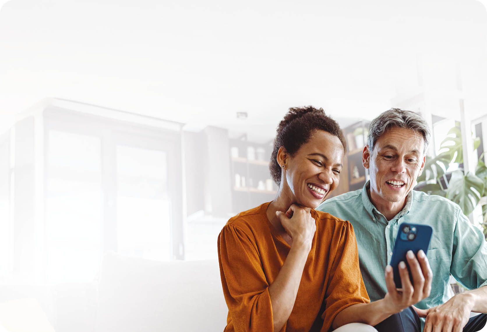 A beautiful African-American woman and a good-looking man sitting in the living room. They are looking at the smart phone and smiling