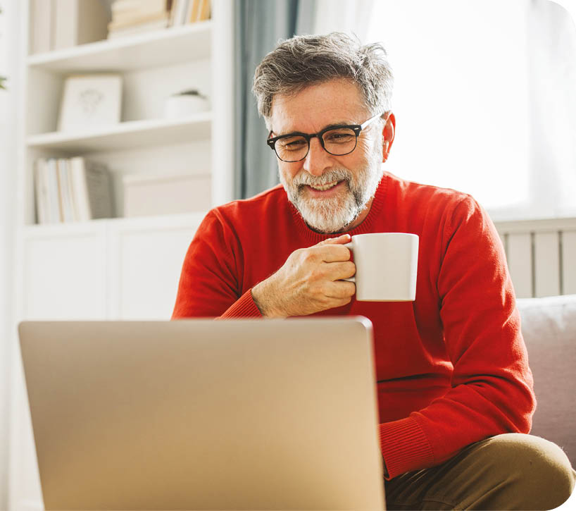 Mature man sitting on sofa at home and using laptop for work.