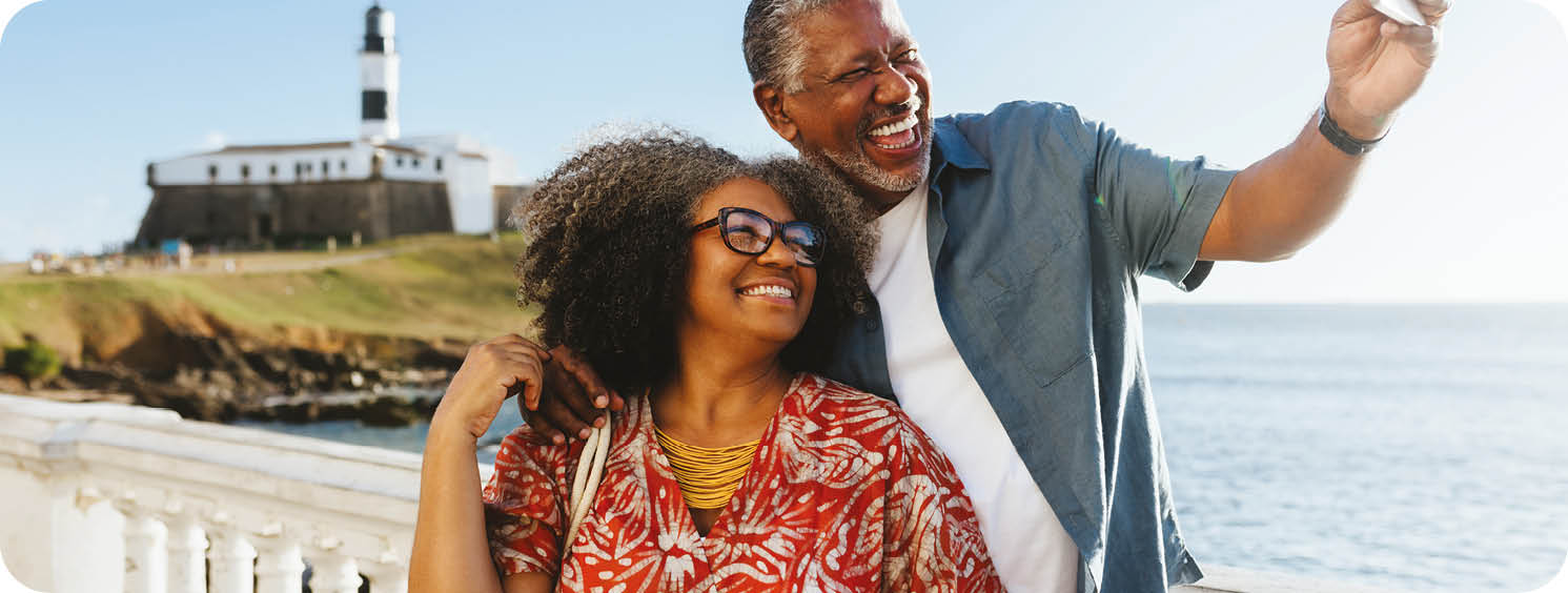 Happy elderly couple taking a selfie near the coast, with the sea and a lighthouse in the background. Retired Life at it's best.
