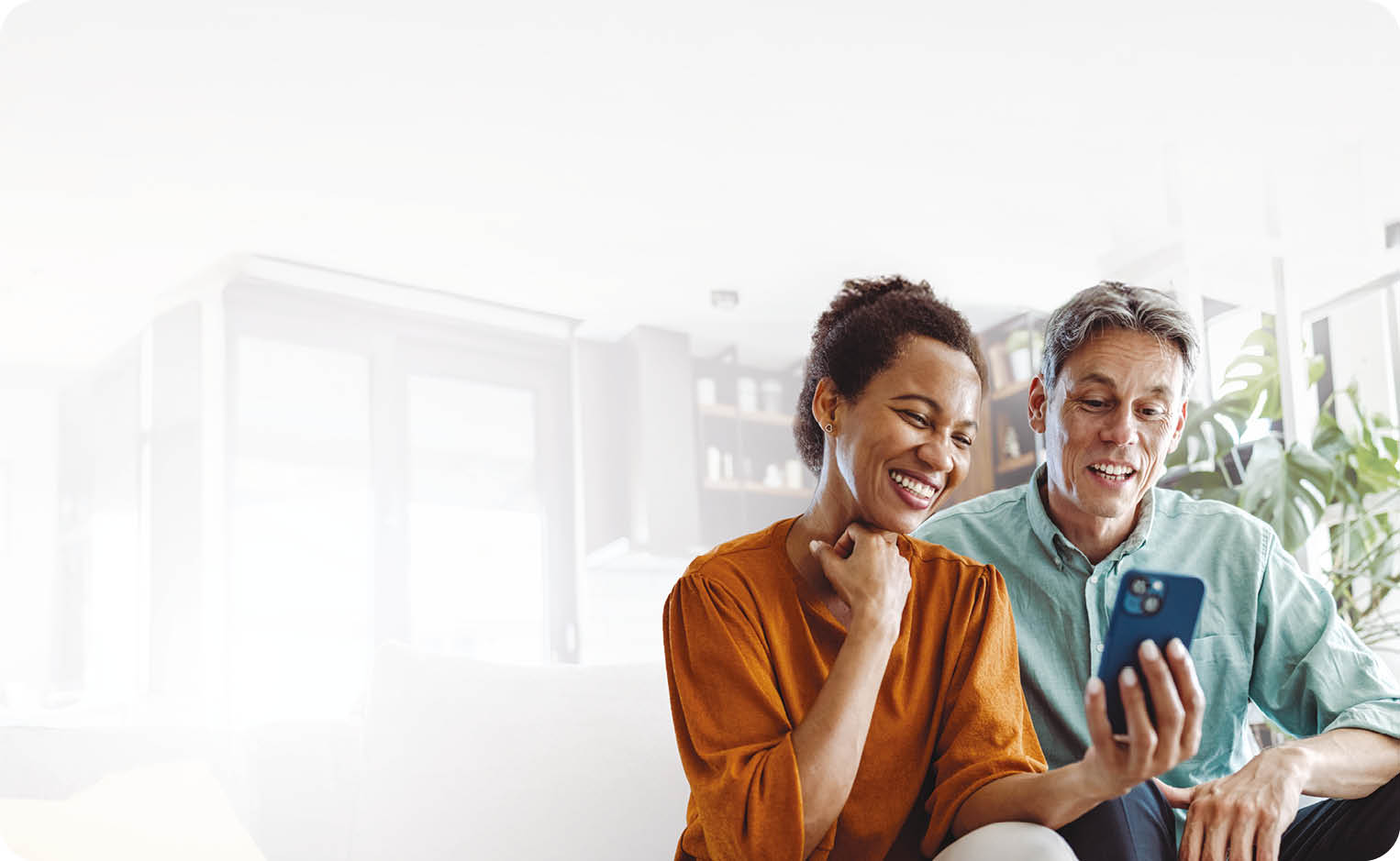 A beautiful African-American woman and a good-looking man sitting in the living room. They are looking at the smart phone and smiling