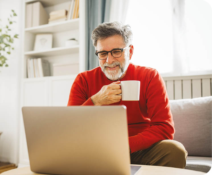 Mature man sitting on sofa at home and using laptop for work.