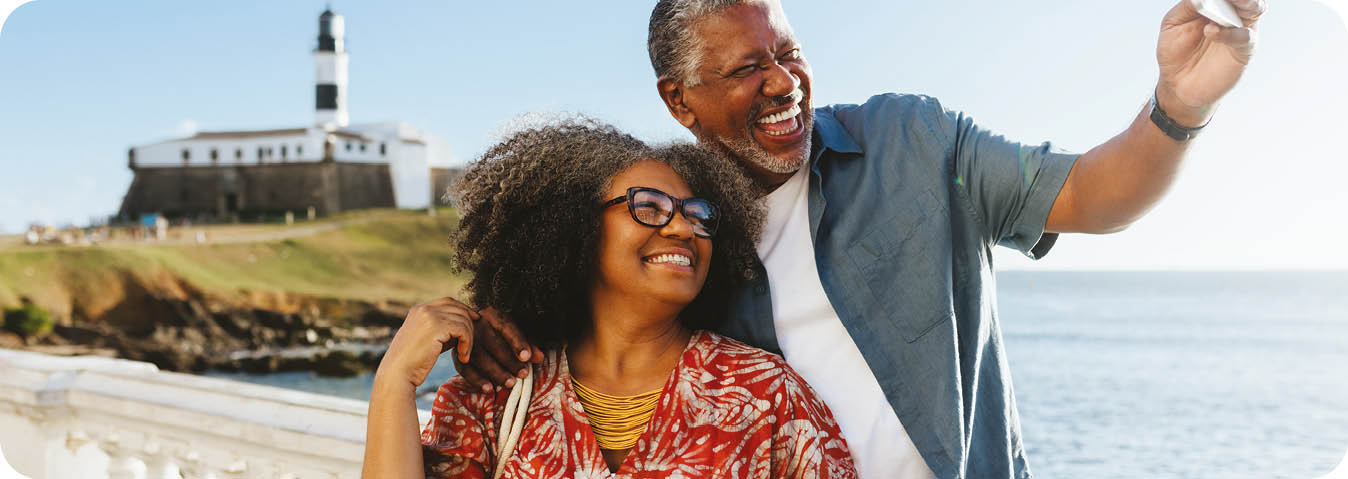 Happy elderly couple taking a selfie near the coast, with the sea and a lighthouse in the background. Retired Life at it's best.