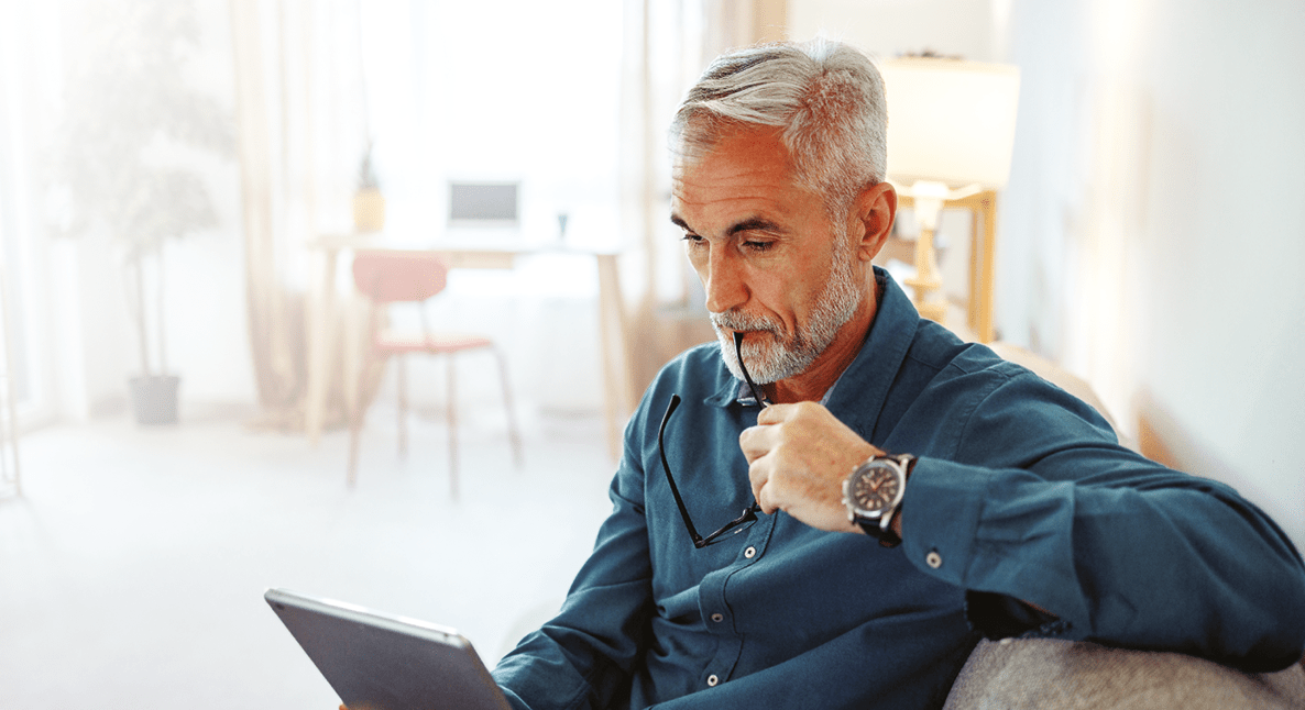 Casually clothed mature man using digital tablet while relaxing on a sofa at home
