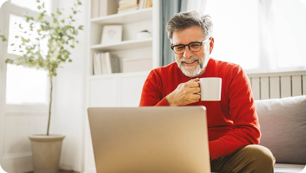 Mature man sitting on sofa at home and using laptop for work.
