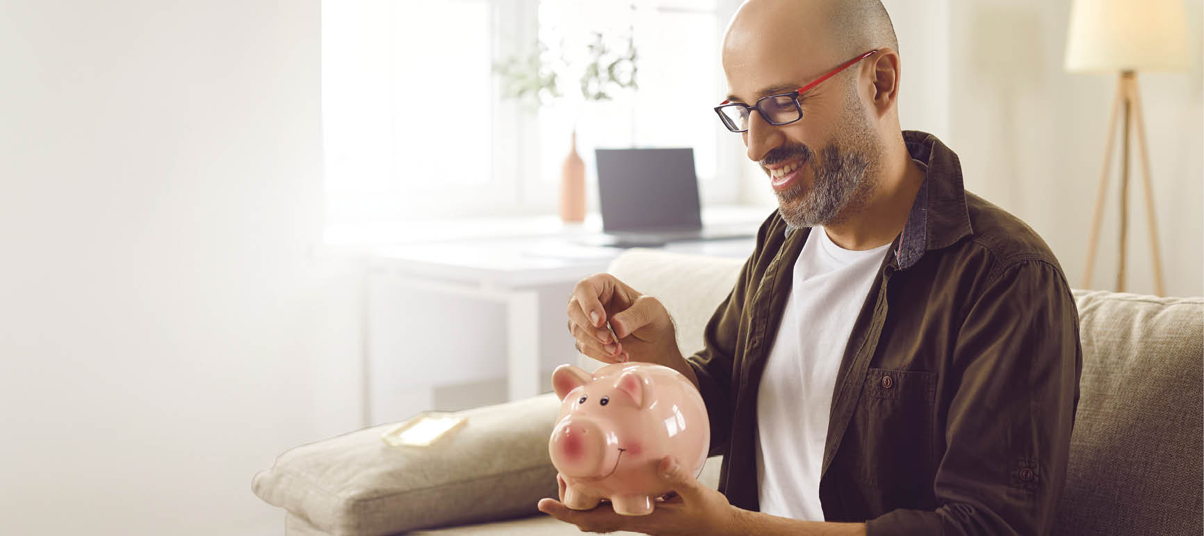 A man sitting on a couch holding a pink piggy bank. Description generated by AI