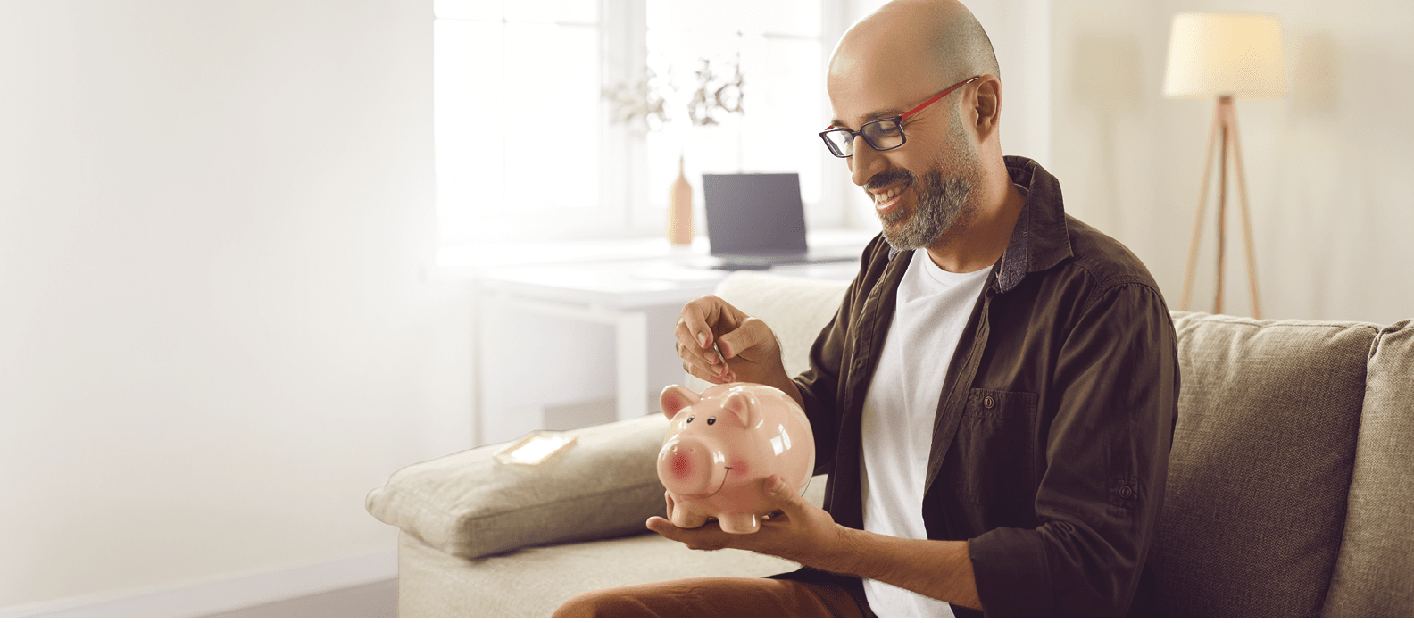 A man sitting on a couch holding a pink piggy bank. Description generated by AI