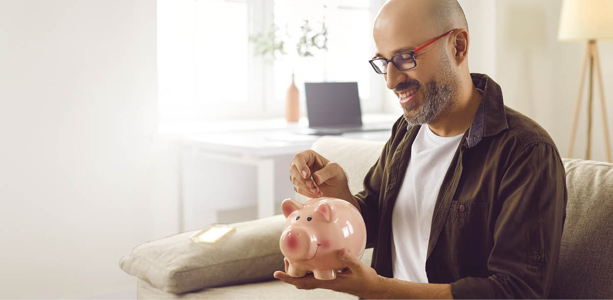 A man sitting on a couch holding a pink piggy bank. Description generated by AI