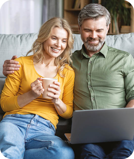 A man and woman sitting on a couch, the woman holding a cup and the man holding a laptop. Description generated by AI