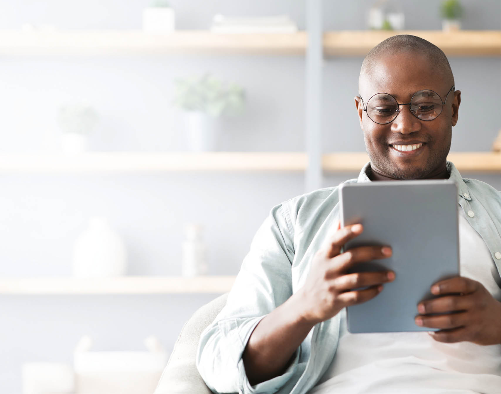 A man in a grey shirt is sitting on a couch and reading a tablet. Description generated by AI