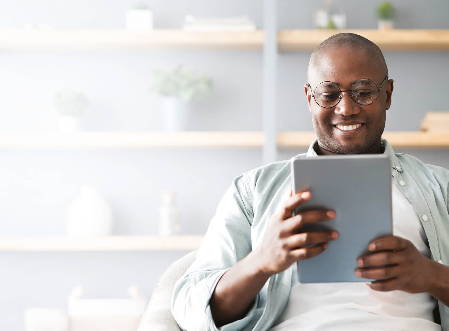 A man in a grey shirt is sitting on a couch and reading a tablet. Description generated by AI