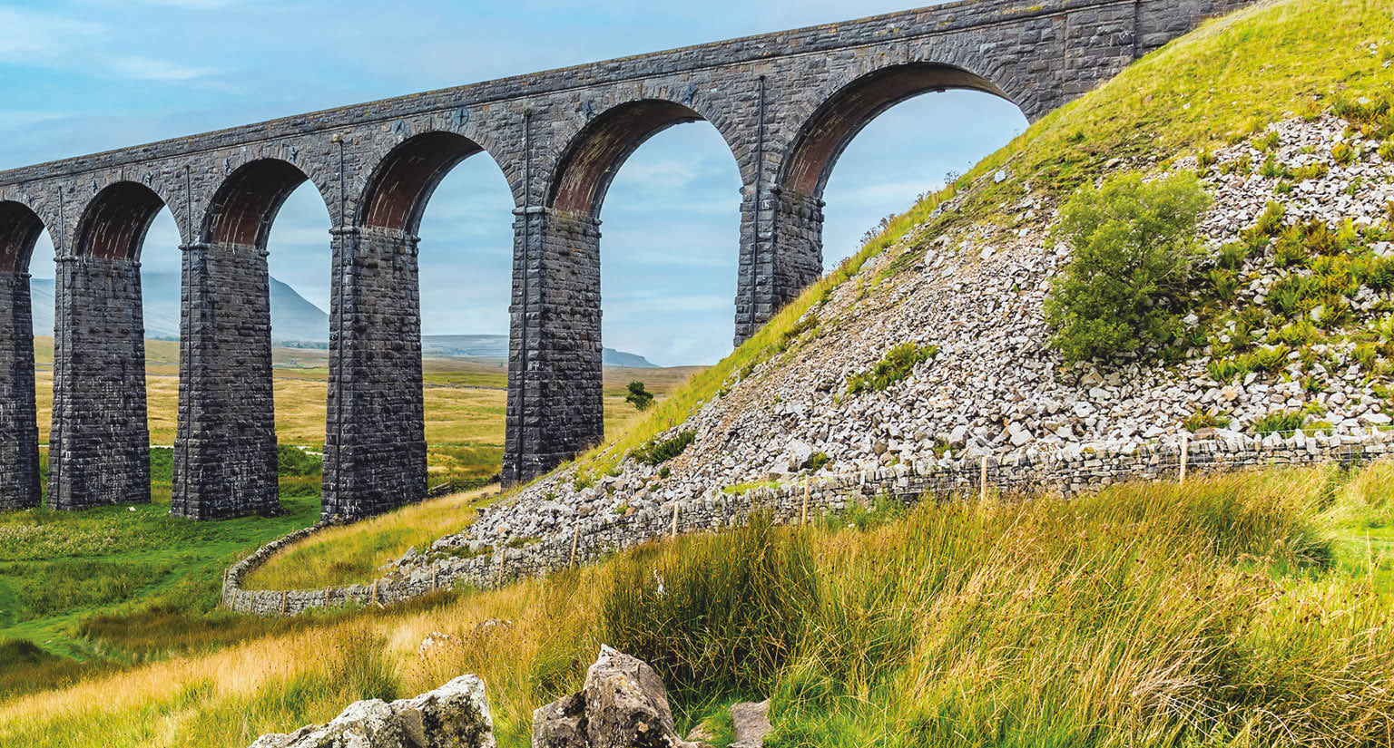 A large stone bridge over a grassy field. Description generated by AI