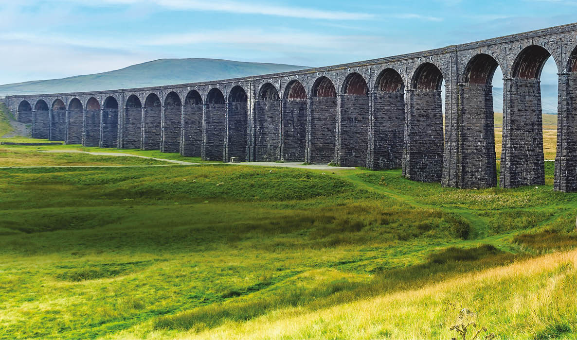 A large stone bridge over a grassy field. Description generated by AI