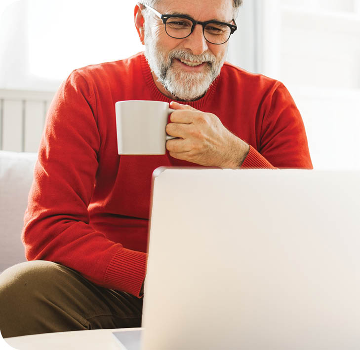 Mature man sitting on sofa at home and using laptop for work.