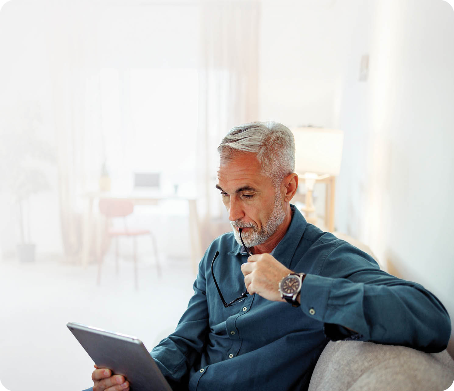 Casually clothed mature man using digital tablet while relaxing on a sofa at home