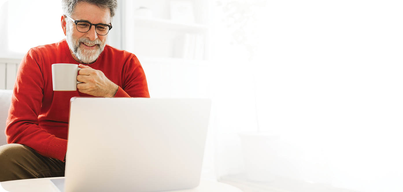 Mature man sitting on sofa at home and using laptop for work.