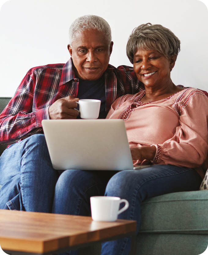 Senior Couple Sitting On Sofa At Home Using Laptop To Shop Online