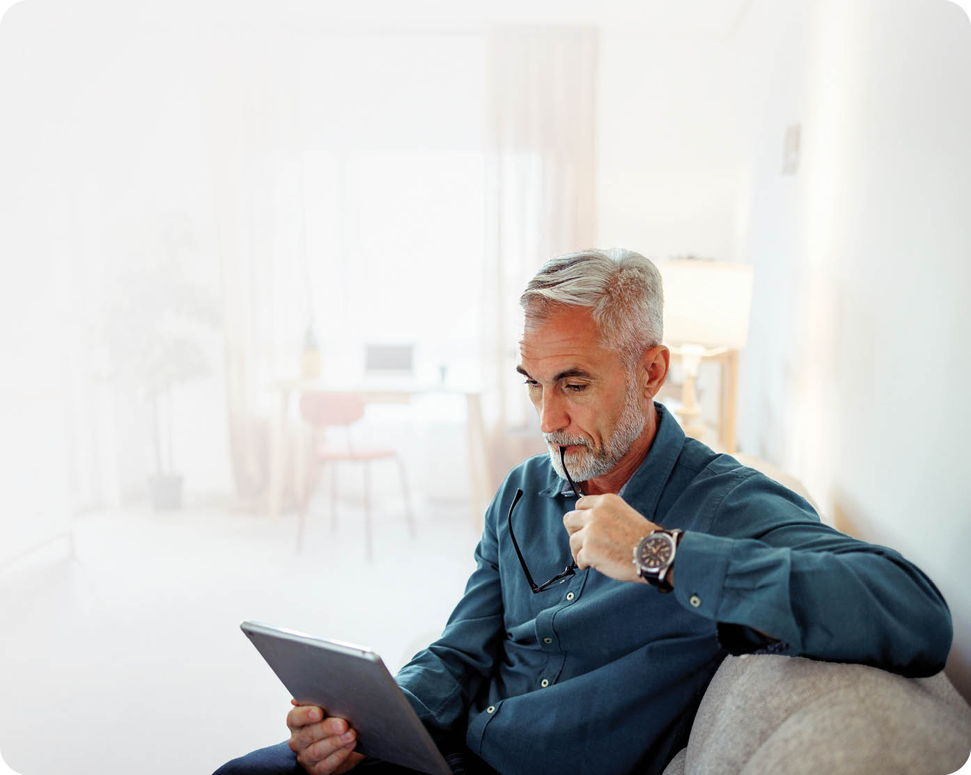 Casually clothed mature man using digital tablet while relaxing on a sofa at home
