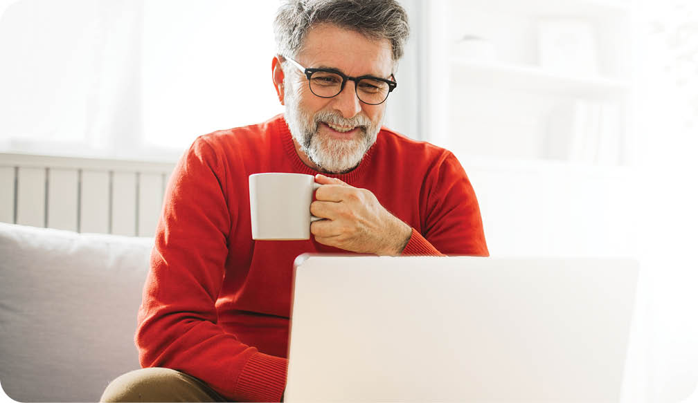 Mature man sitting on sofa at home and using laptop for work.