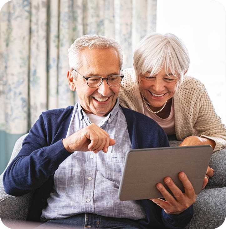 An older man and woman are sitting on a couch, looking at a tablet computer together. AI generated content