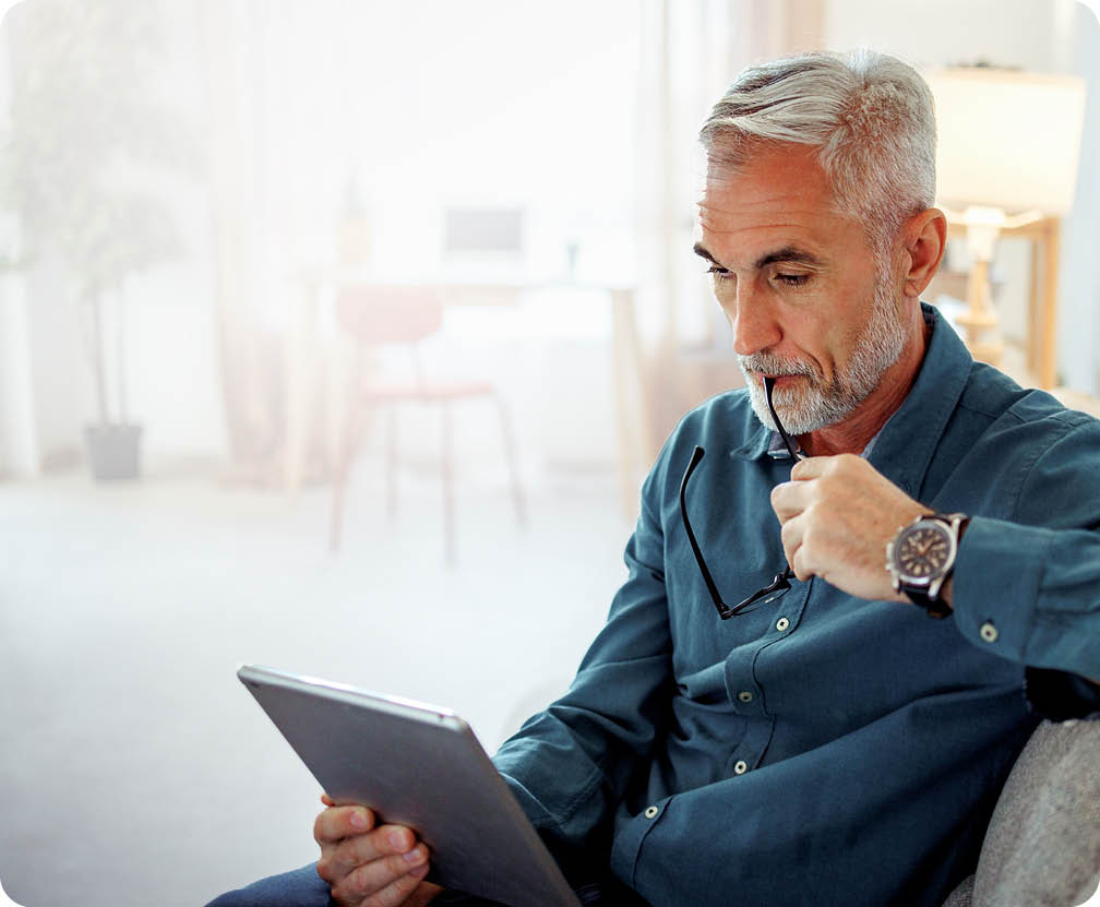 Casually clothed mature man using digital tablet while relaxing on a sofa at home