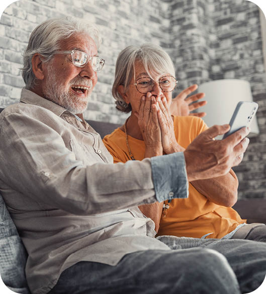 An elderly man and woman are sitting on a couch, looking at a cell phone. AI generated content