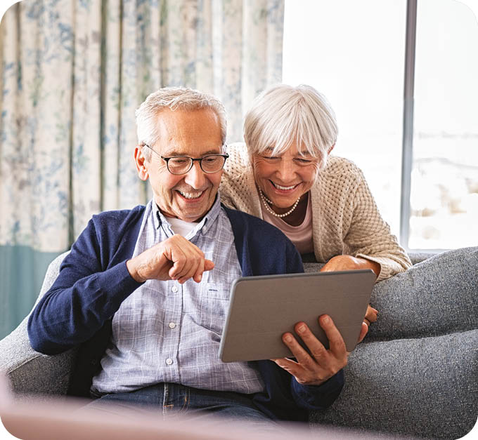 An older man and woman are sitting on a couch, looking at a tablet computer together. AI generated content