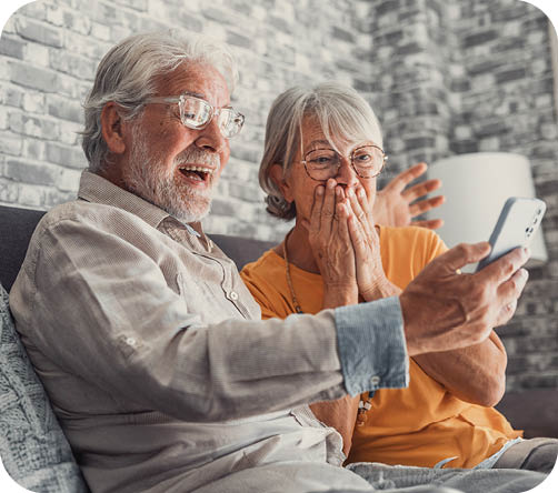 An elderly man and woman are sitting on a couch, looking at a cell phone. AI generated content