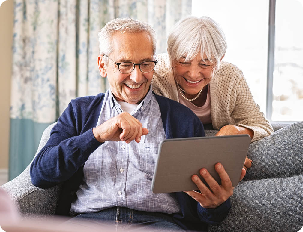 An older man and woman are sitting on a couch, looking at a tablet computer together. AI generated content