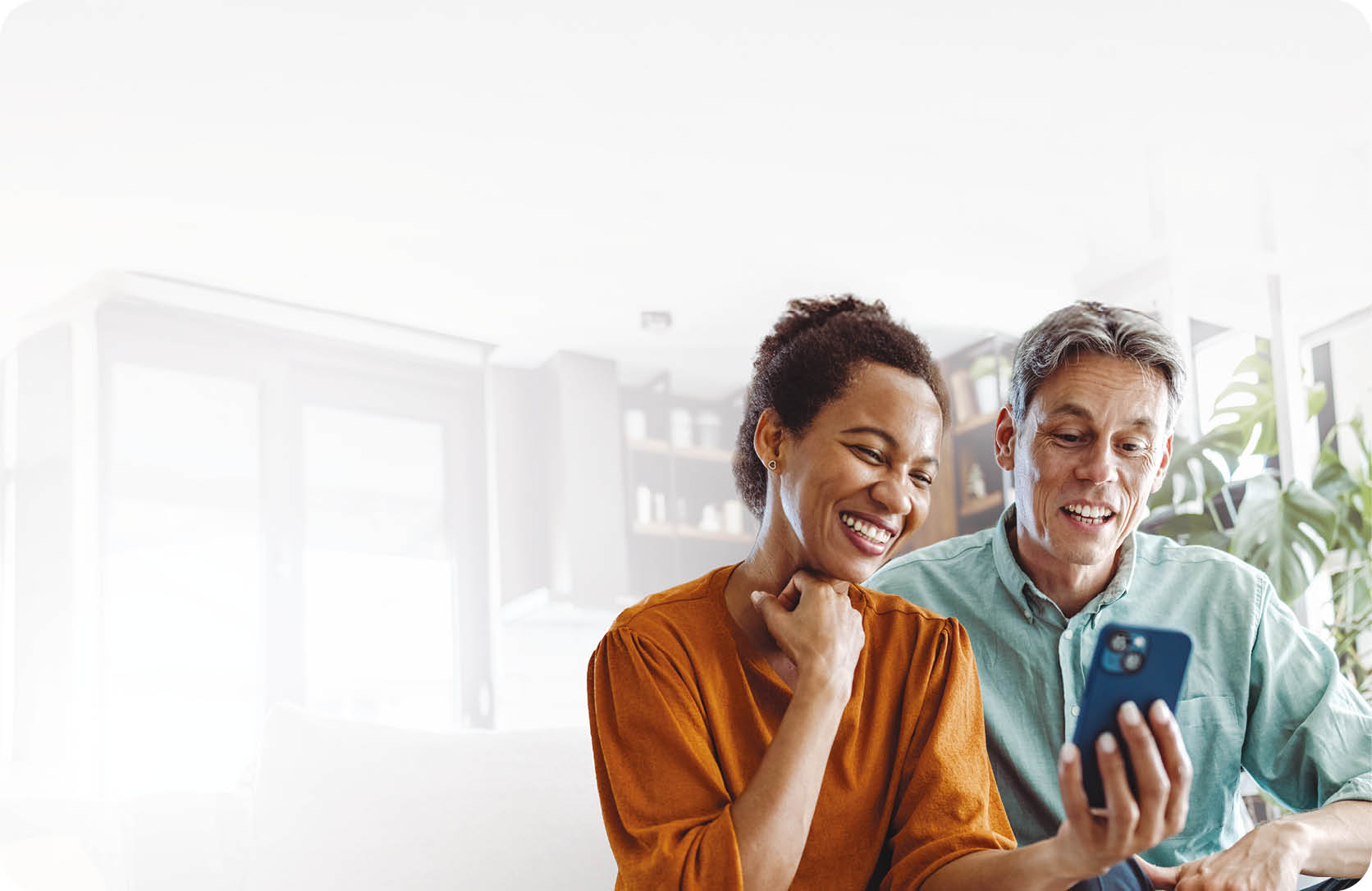 A beautiful African-American woman and a good-looking man sitting in the living room. They are looking at the smart phone and smiling