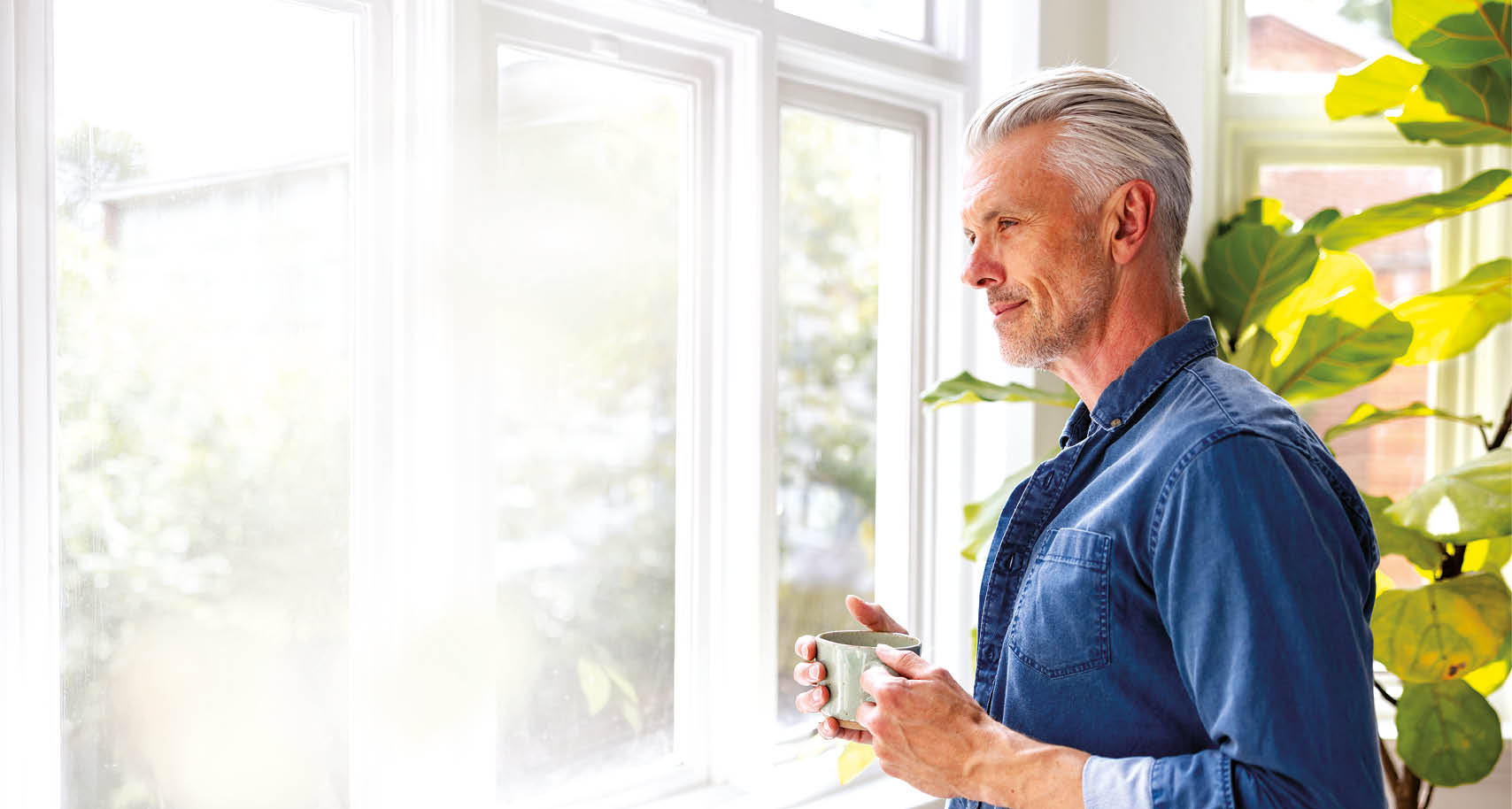 Happy man at home drinking a cup of coffee while looking through the window - domestic life concepts