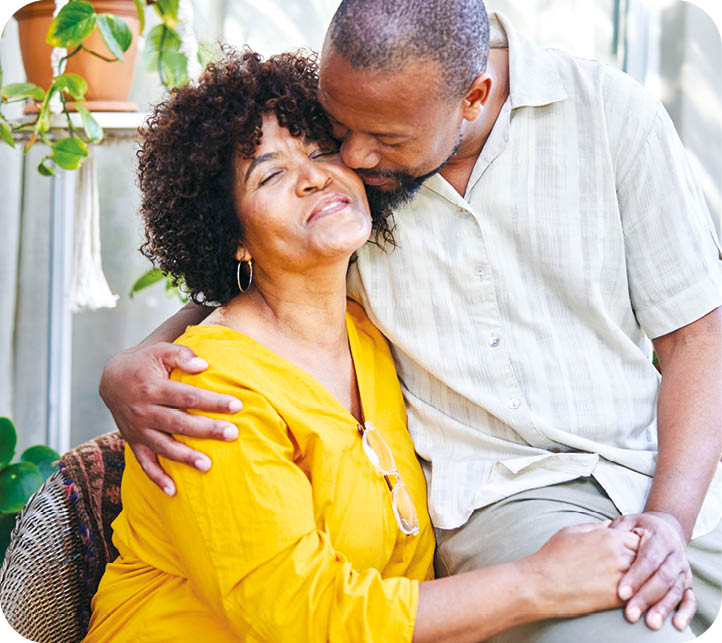 Loving mature man kissing his smiling wife on the cheek while sitting together outside on their patio at home in summer