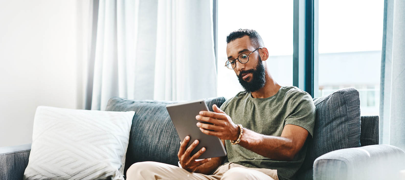 Shot of a handsome young man using his digital tablet while sitting on a sofa at home