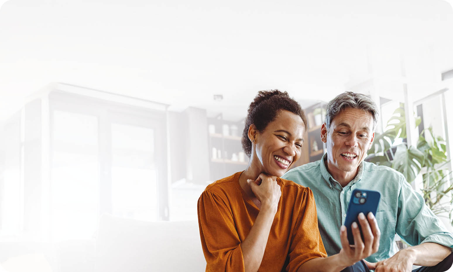 A beautiful African-American woman and a good-looking man sitting in the living room. They are looking at the smart phone and smiling