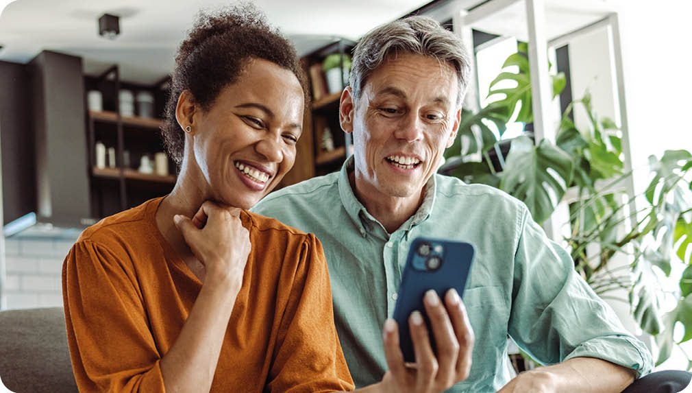 A beautiful African-American woman and a good-looking man sitting in the living room. They are looking at the smart phone and smiling