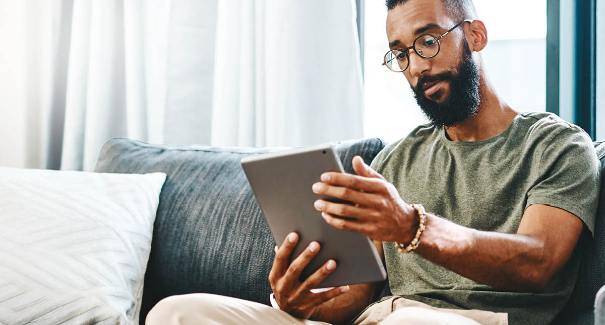 Shot of a handsome young man using his digital tablet while sitting on a sofa at home