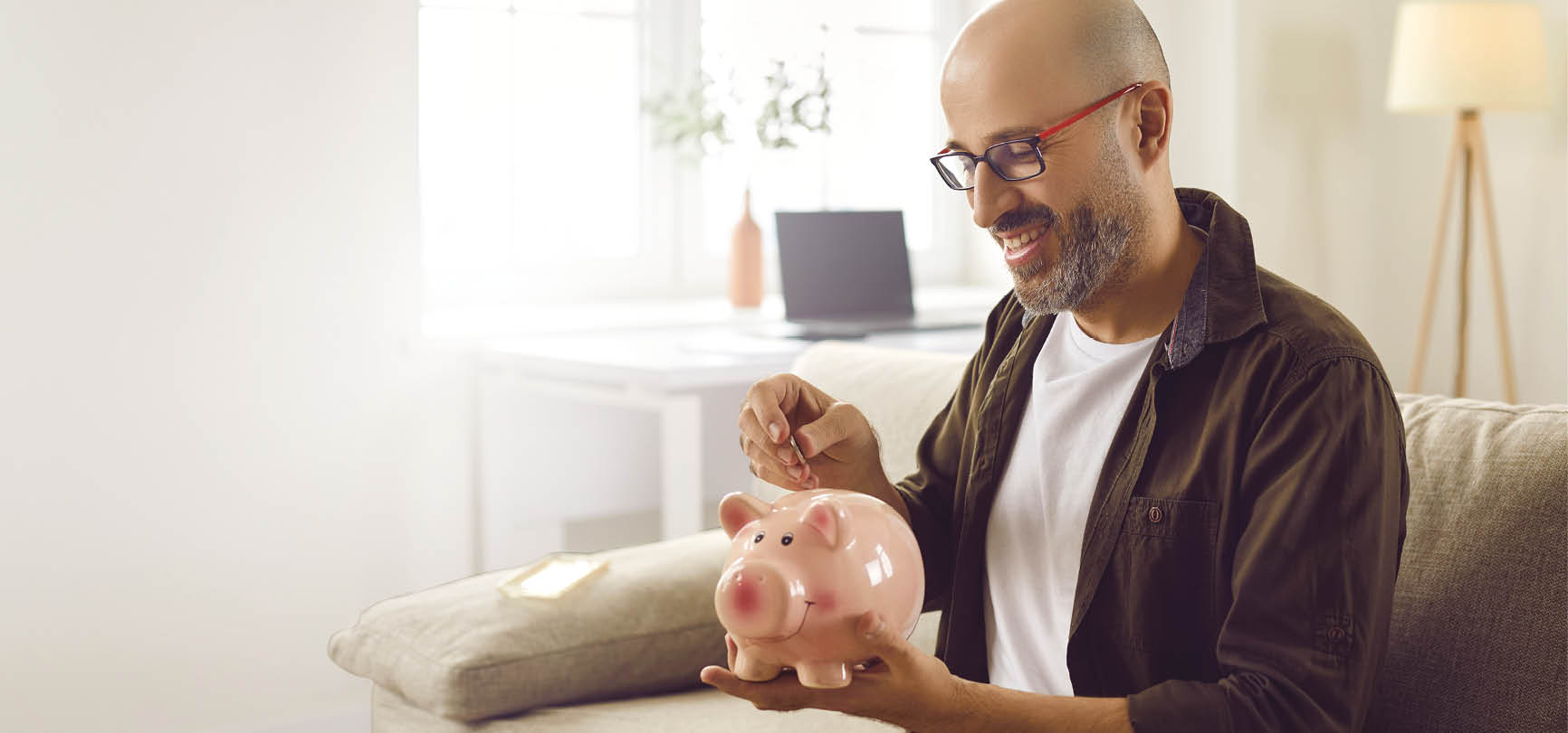 A man sitting on a couch holding a pink piggy bank. Description generated by AI