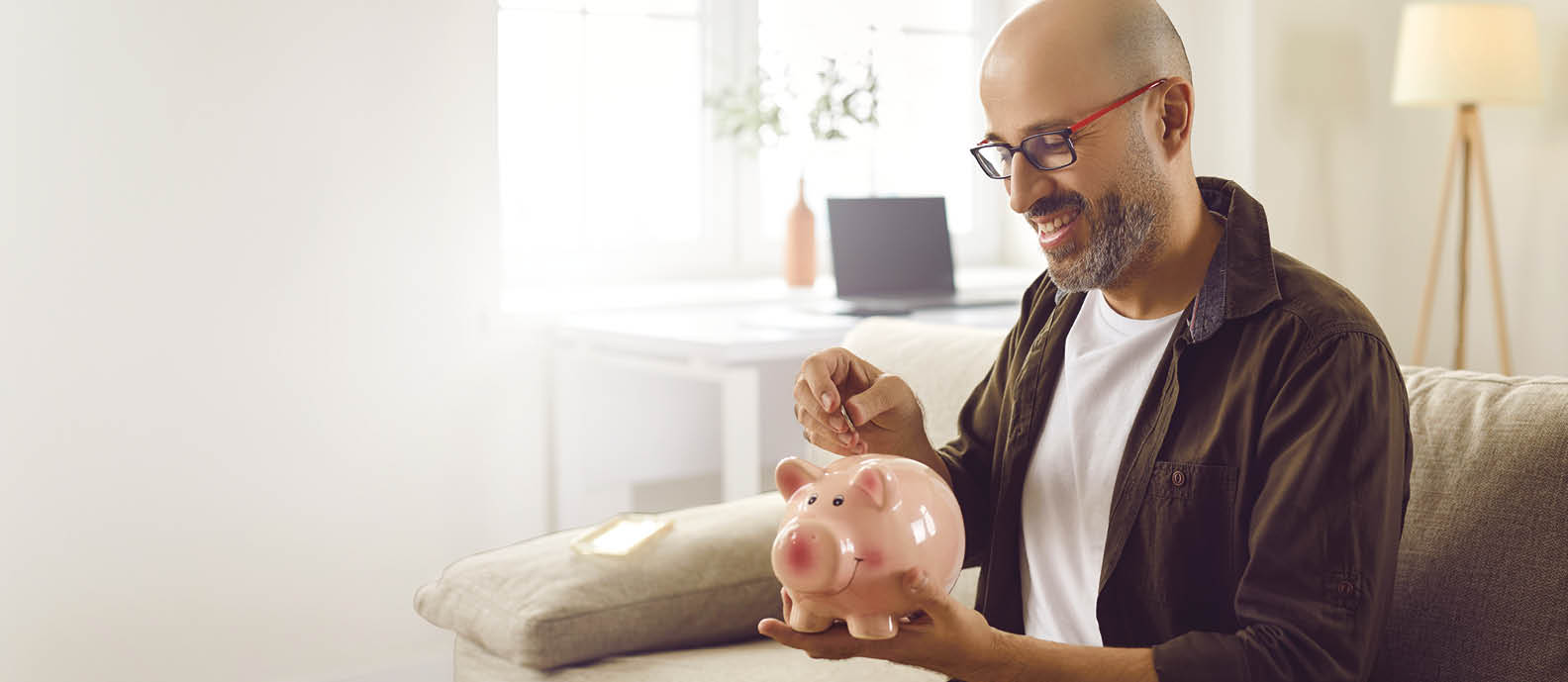 A man sitting on a couch holding a pink piggy bank. Description generated by AI