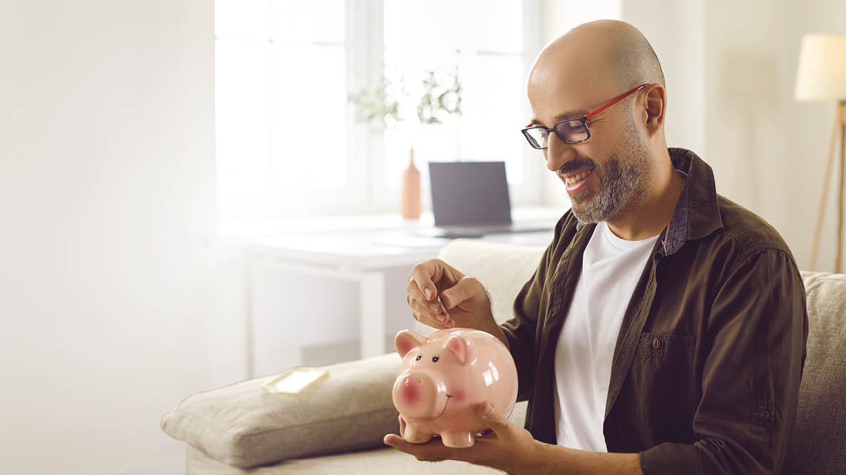 A man sitting on a couch holding a pink piggy bank. Description generated by AI