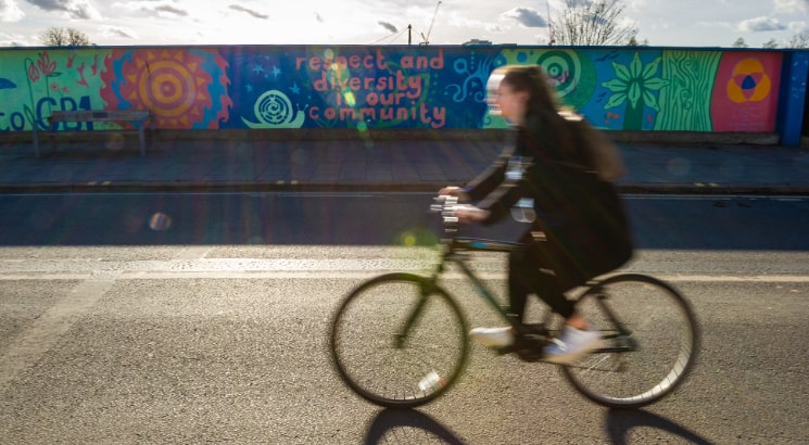 A cyclist moving past a hoarding that says respect and diversity in our community. Image by Matthew Power Photography.