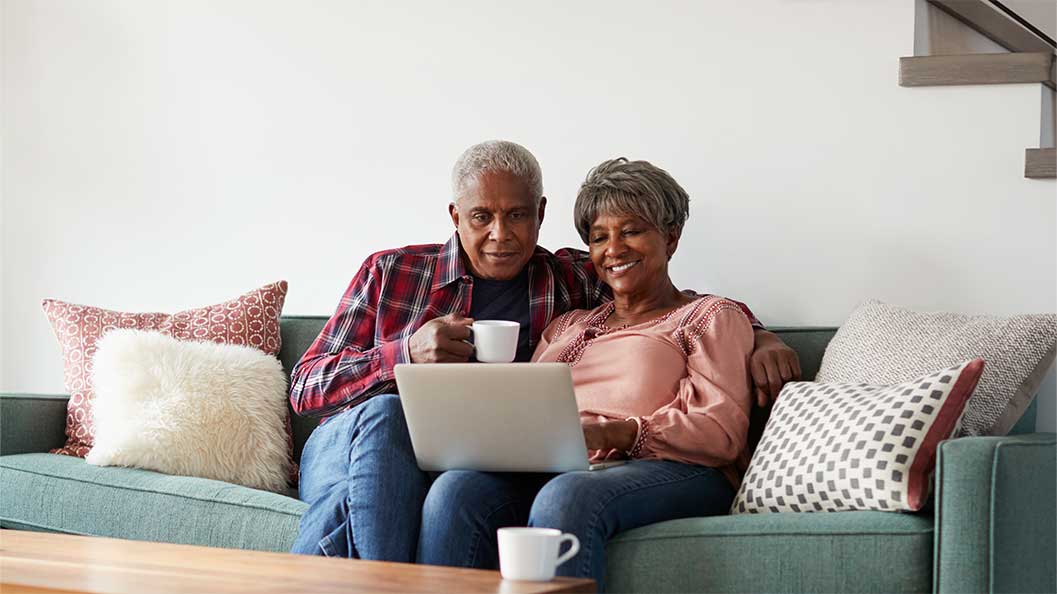 A couple sat on a sofa looking at laptop