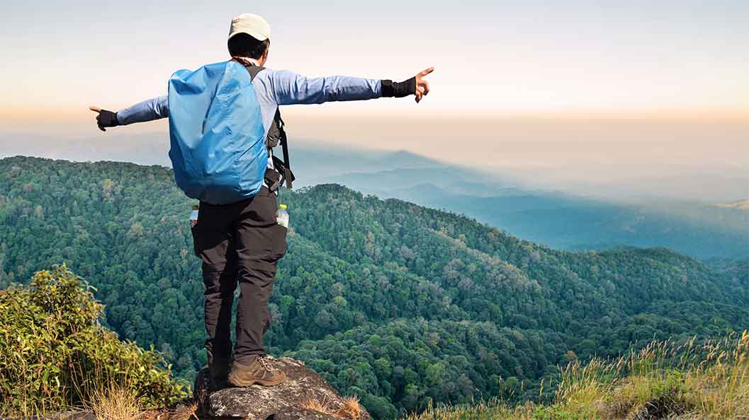 A man with a blue backpack and a white hat on a hill